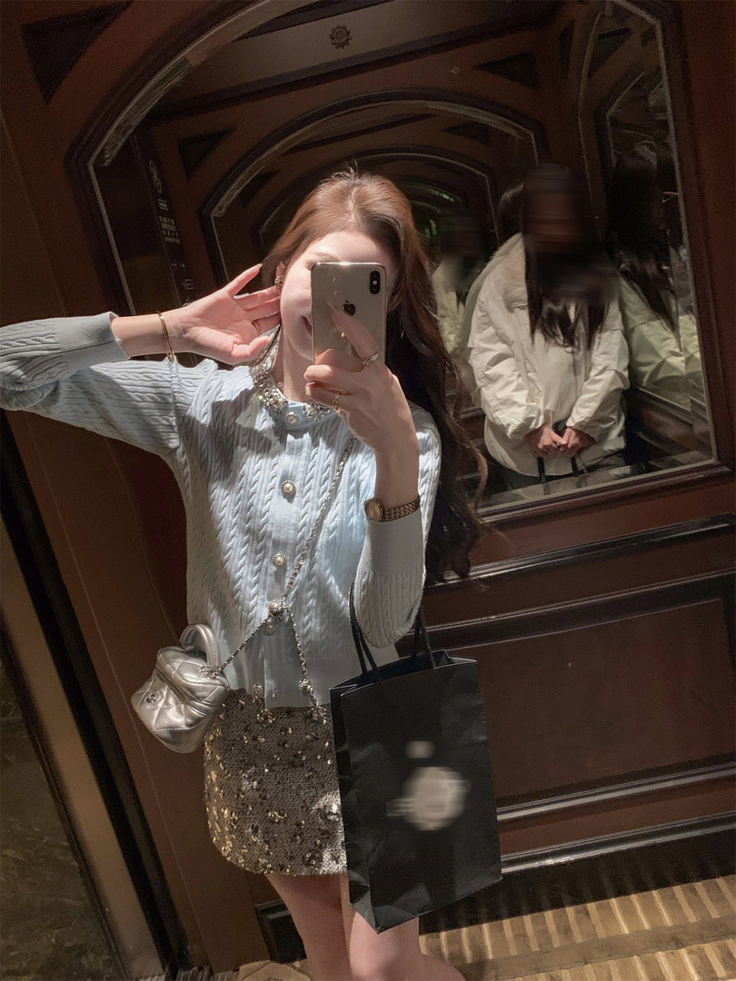 Woman taking a mirror selfie wearing a light blue knit top and gold sequin mini skirt with accessories