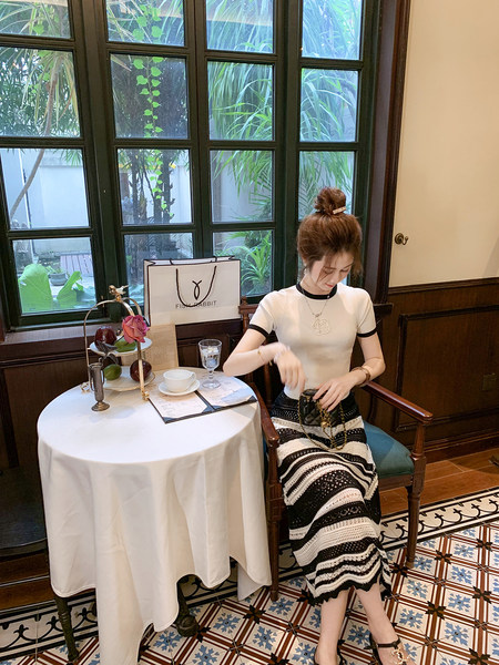 Woman wearing a white fitted short-sleeve top with black trim and a black-and-white patterned skirt
