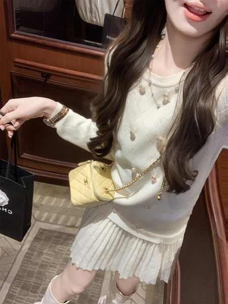 Woman wearing a white knit sweater and pleated skirt with a small yellow quilted handbag