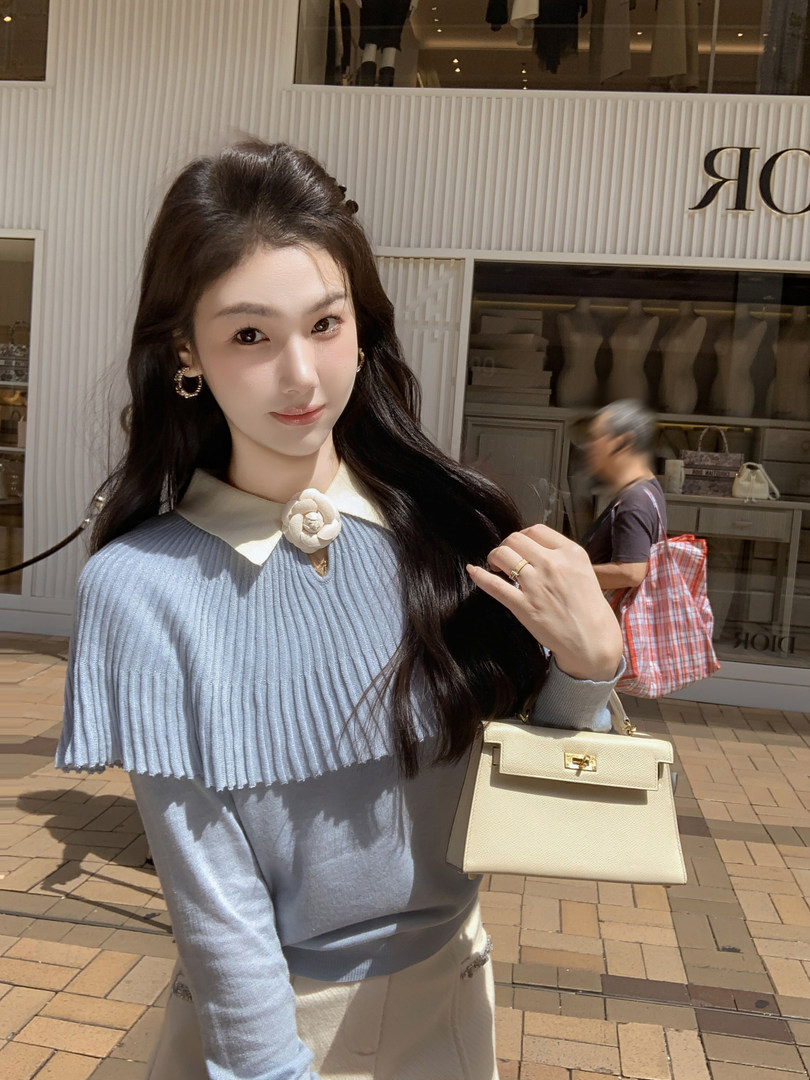 Woman wearing a light blue ribbed knit top and holding a cream handbag