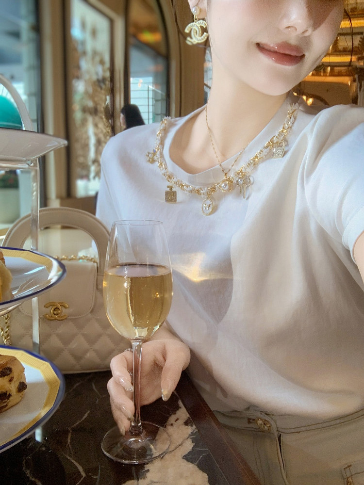 Woman wearing a white top with layered gold jewelry in a luxe cafe setting