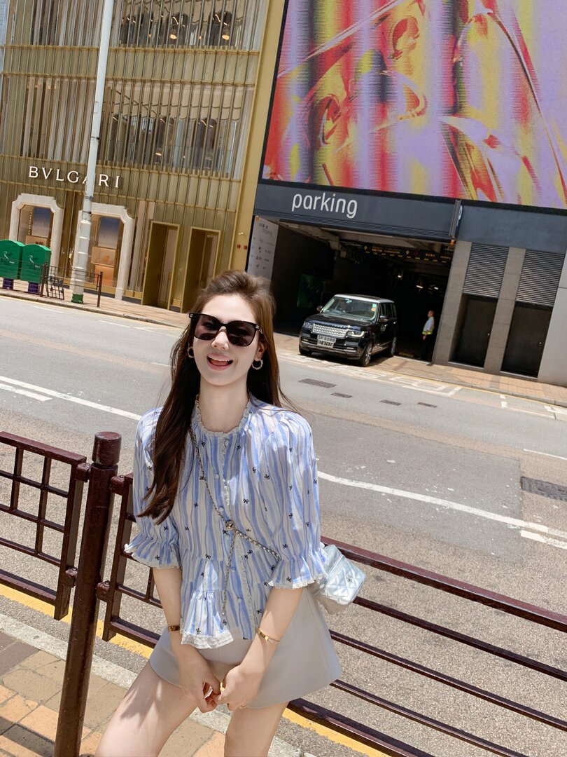 Woman wearing a light blue striped blouse and beige shorts outdoors