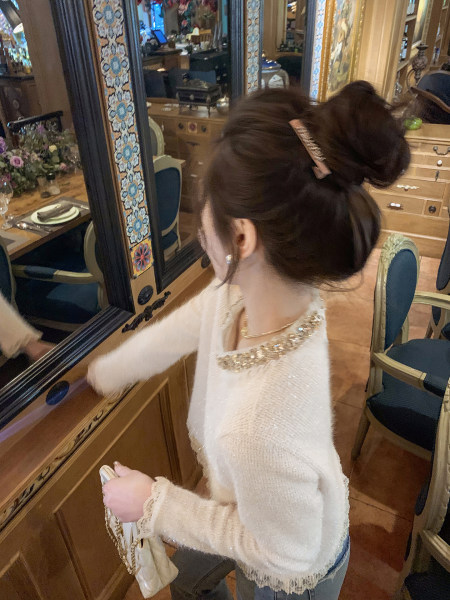 Woman wearing a white textured sweater with decorative neckline and holding a small handbag