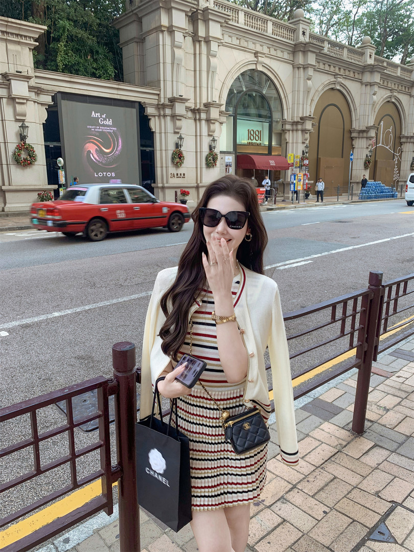 Woman wearing a striped dress with a cream cardigan and black quilted mini bag on a city street.