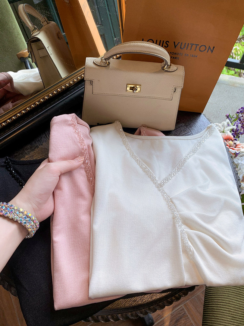 A cream handbag with folded pink and white clothing displayed on a table