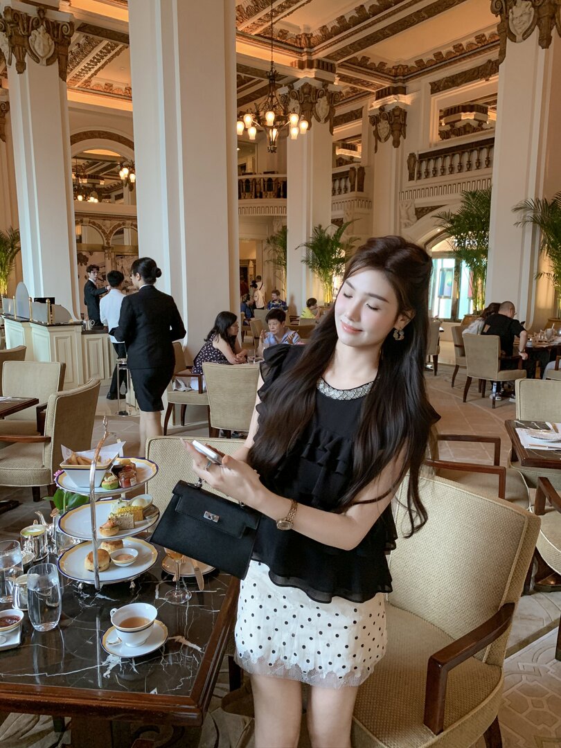 Woman wearing a black top and white polka dot skirt with a black handbag in a restaurant