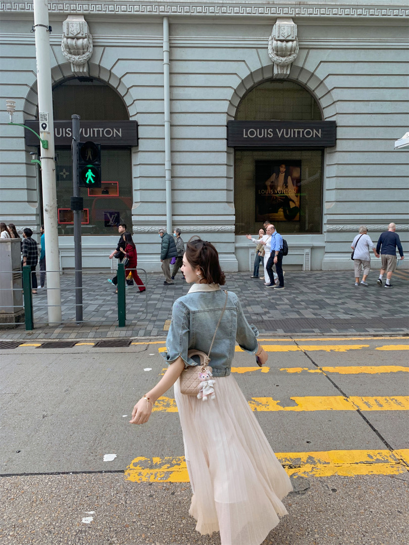 Woman wearing a light denim jacket with a flowing cream skirt and quilted crossbody bag on a city street
