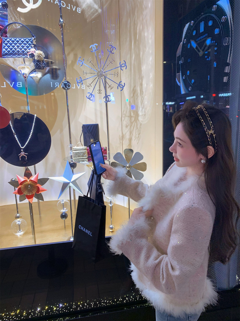 Woman wearing a light pink fuzzy sweater with white fur trim in front of a luxury store display