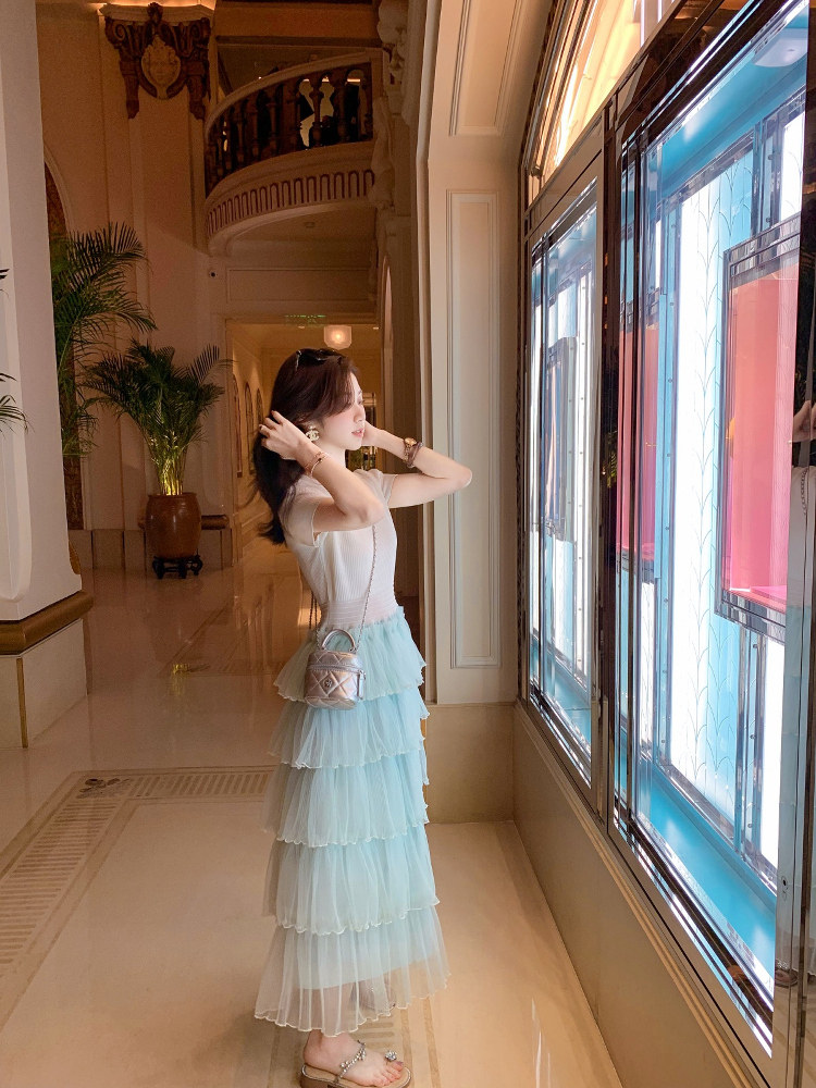 Woman wearing a white top with a light blue tiered tulle skirt and small handbag