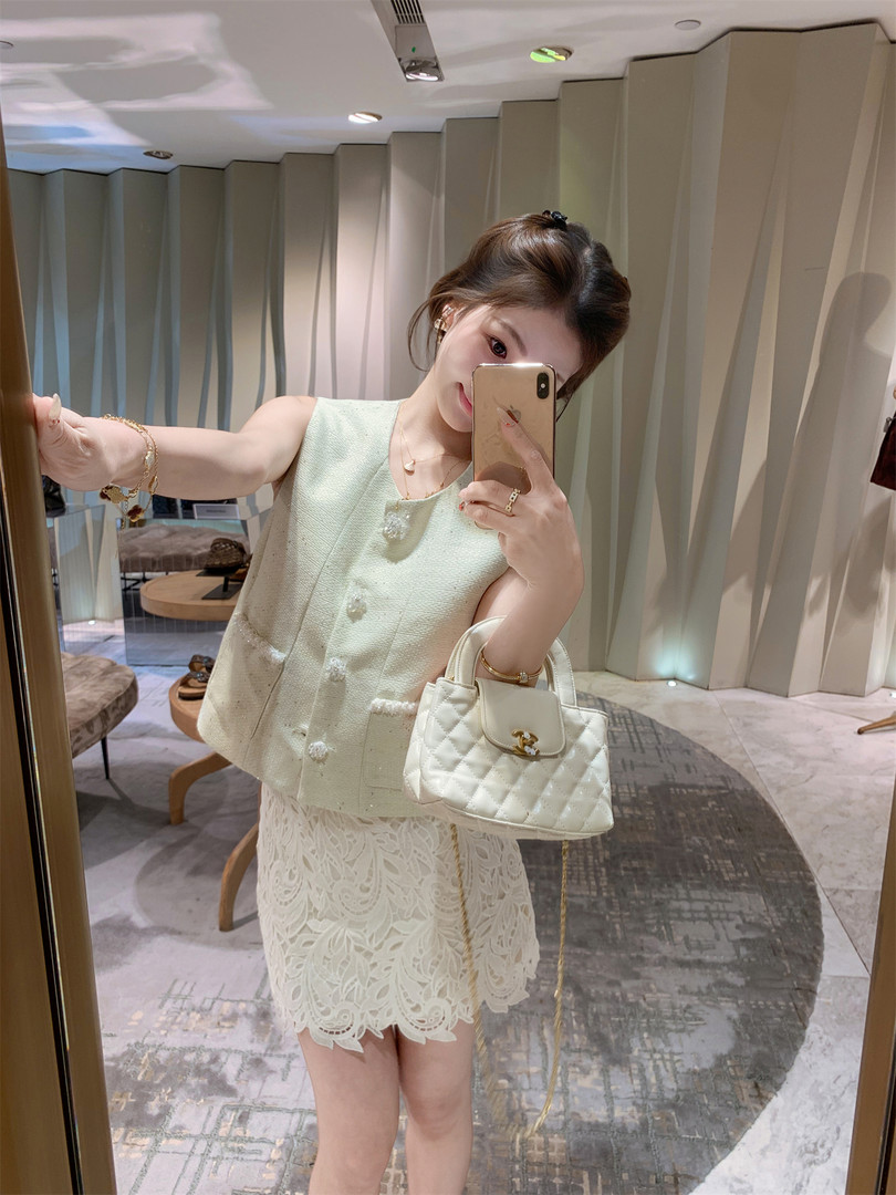 Woman wearing a cream textured sleeveless top and lace skirt with a quilted white handbag