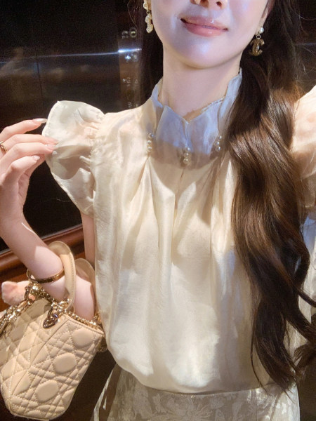 Woman wearing a cream puff-sleeve blouse and holding a quilted handbag