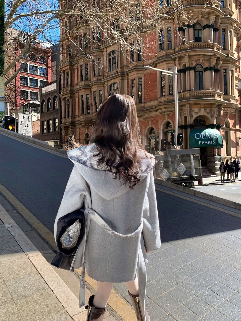 Back view of a woman wearing a gray hooded cape-style coat outdoors
