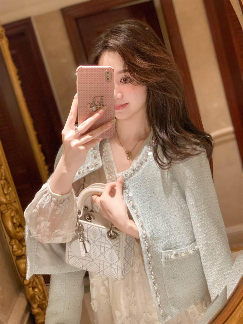 Woman wearing a light blue embellished jacket with a white handbag in a mirror selfie
