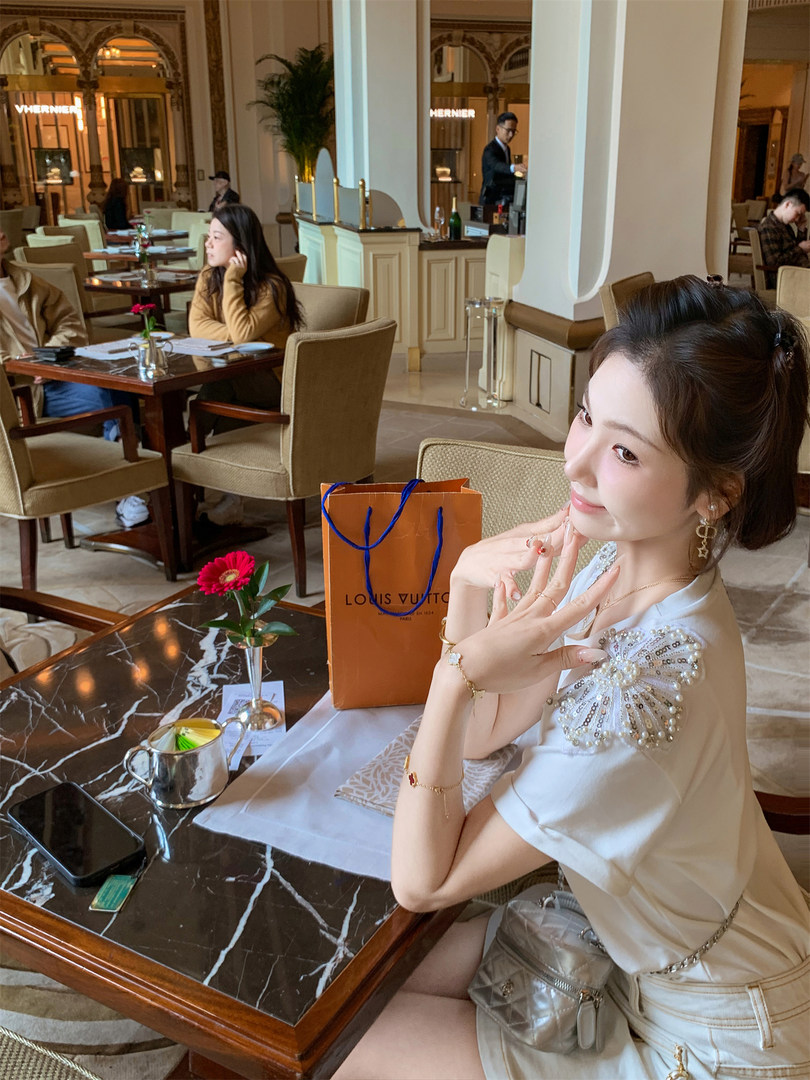 Woman wearing a white embellished top and metallic skirt at a luxury restaurant with a Louis Vuitton shopping bag