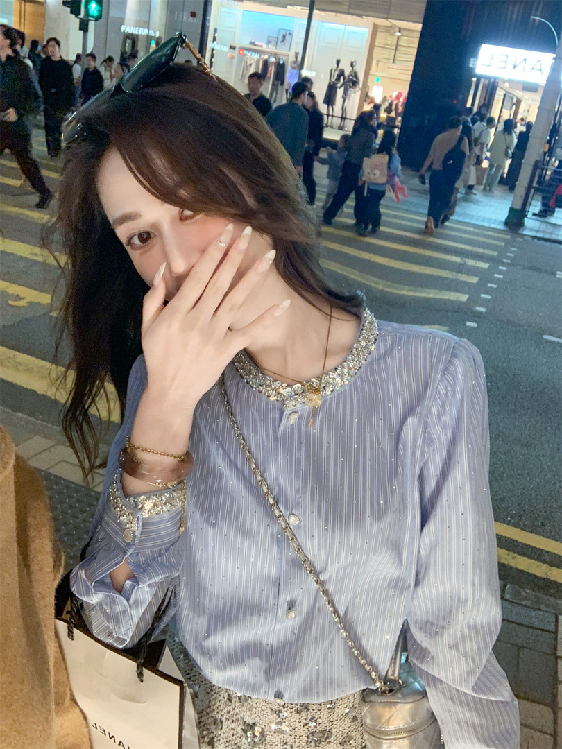Woman wearing a shiny striped embellished blouse with a chain-strap bag at night
