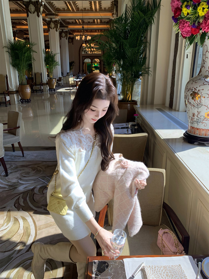 Woman wearing a white lace-trim knit dress with boots and a small quilted handbag in a luxury restaurant