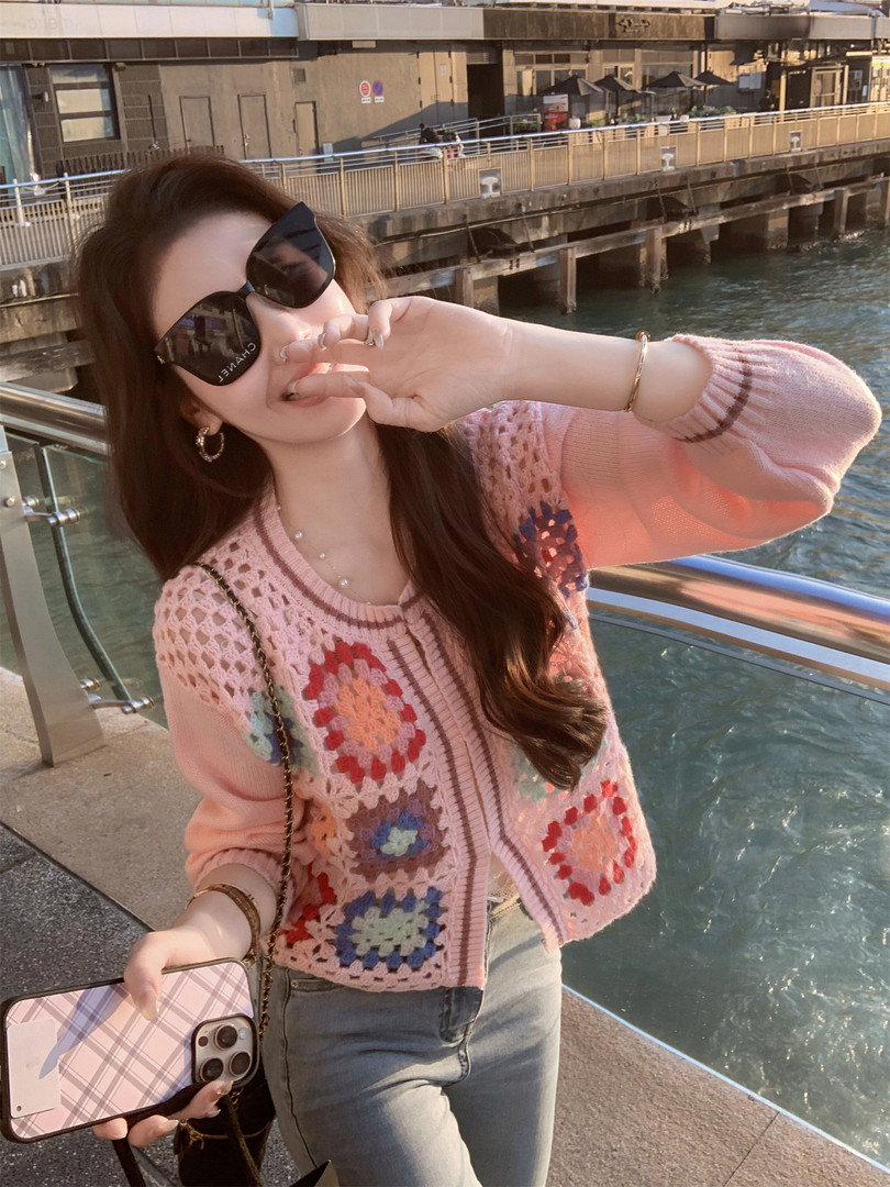 Woman wearing a pink crochet cardigan and sunglasses outdoors by the water