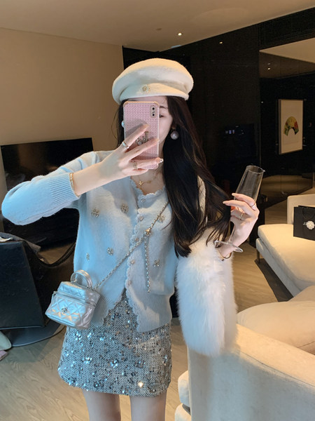 Woman wearing a light blue embellished cardigan and silver sequined skirt with a white beret
