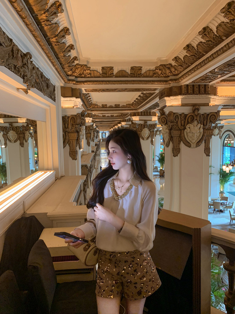 Woman wearing a beige blouse and gold sequin shorts in an ornate indoor setting