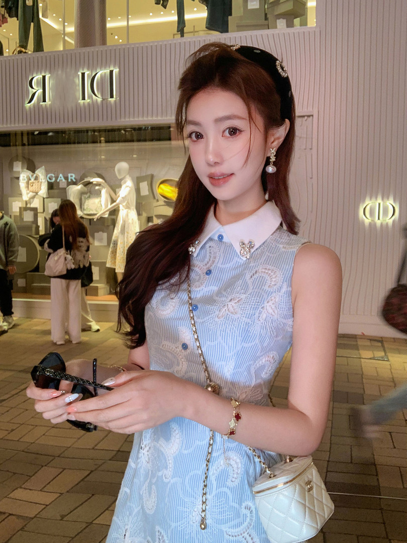 Woman wearing a light blue sleeveless lace dress with a white collar and quilted mini handbag