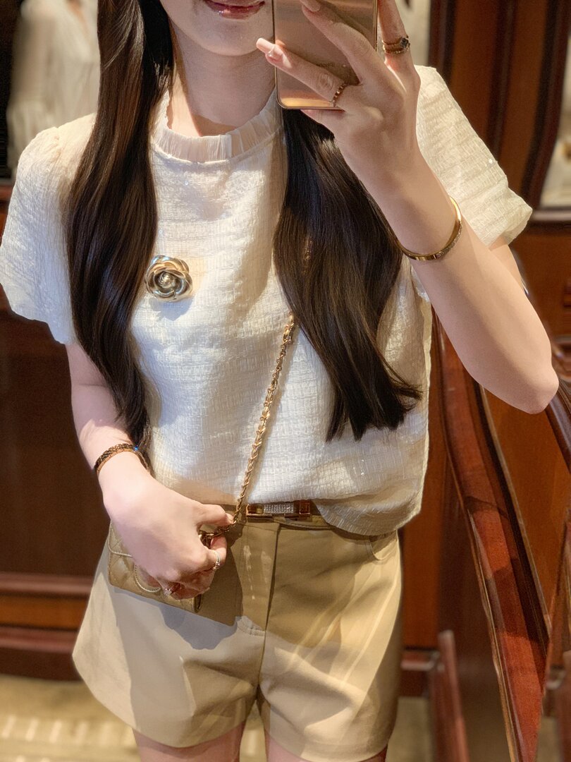 Model wearing a white textured short-sleeve top with beige shorts and a small chain bag