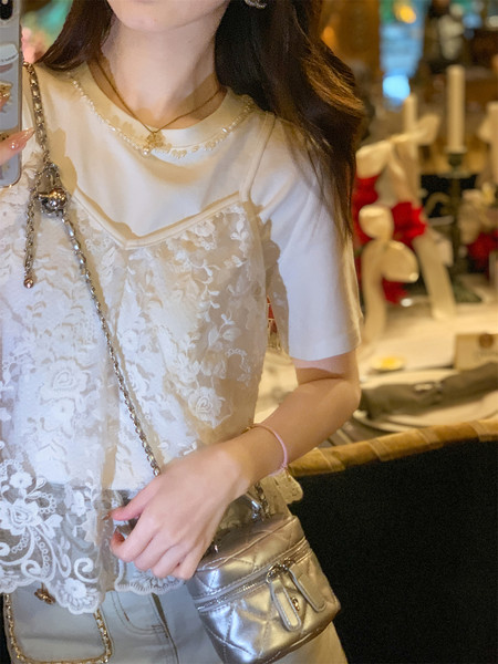 Woman wearing a white lace camisole layered over a white T-shirt with a silver crossbody bag