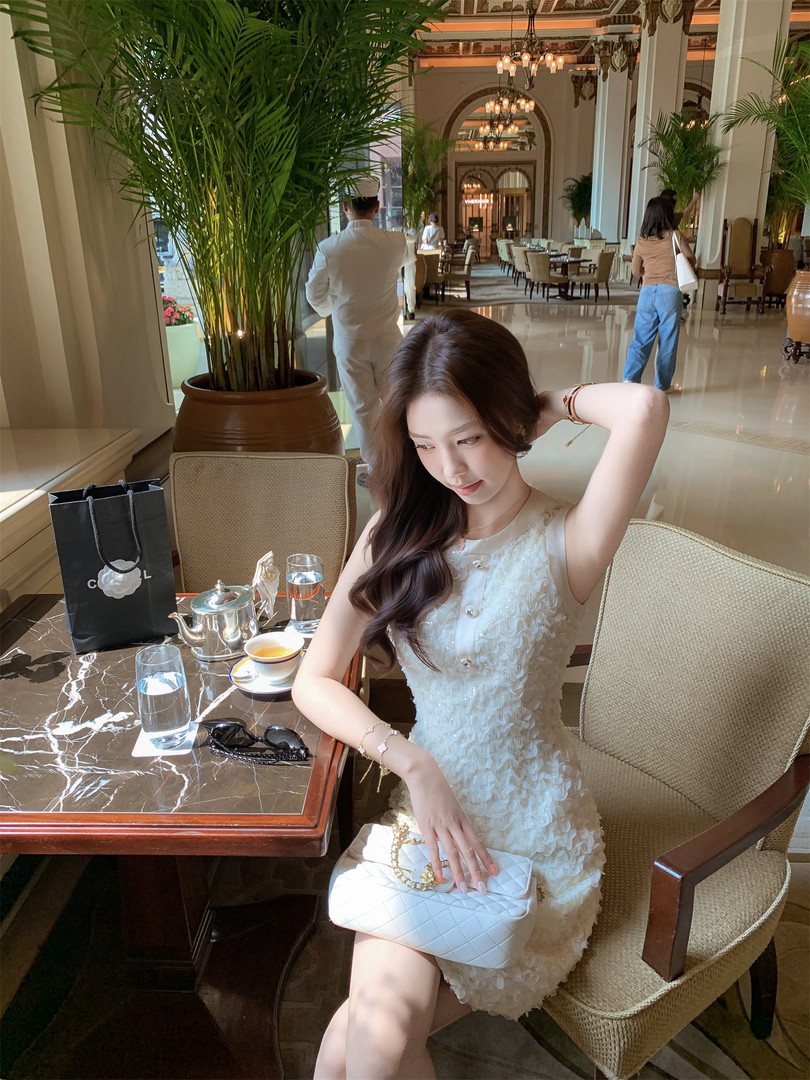 Woman wearing a white textured sleeveless dress seated in a luxury restaurant