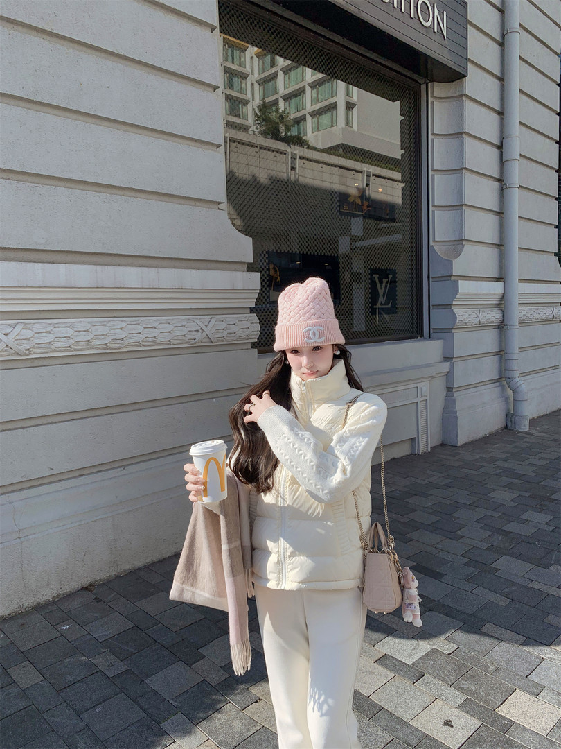 Woman wearing a cream winter outfit with pink knit beanie and scarf, holding a drink outdoors