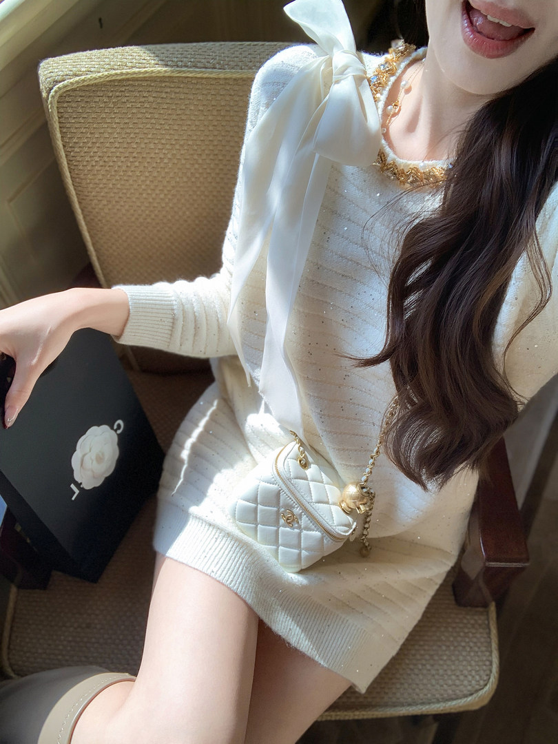 Woman wearing a white embellished knit dress with a ribbon bow and quilted chain handbag