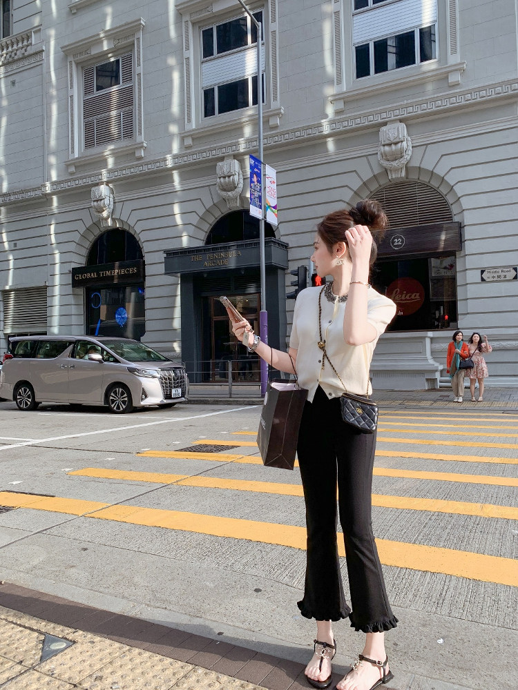Woman wearing a chic cream top with black pants and sandals on a city street