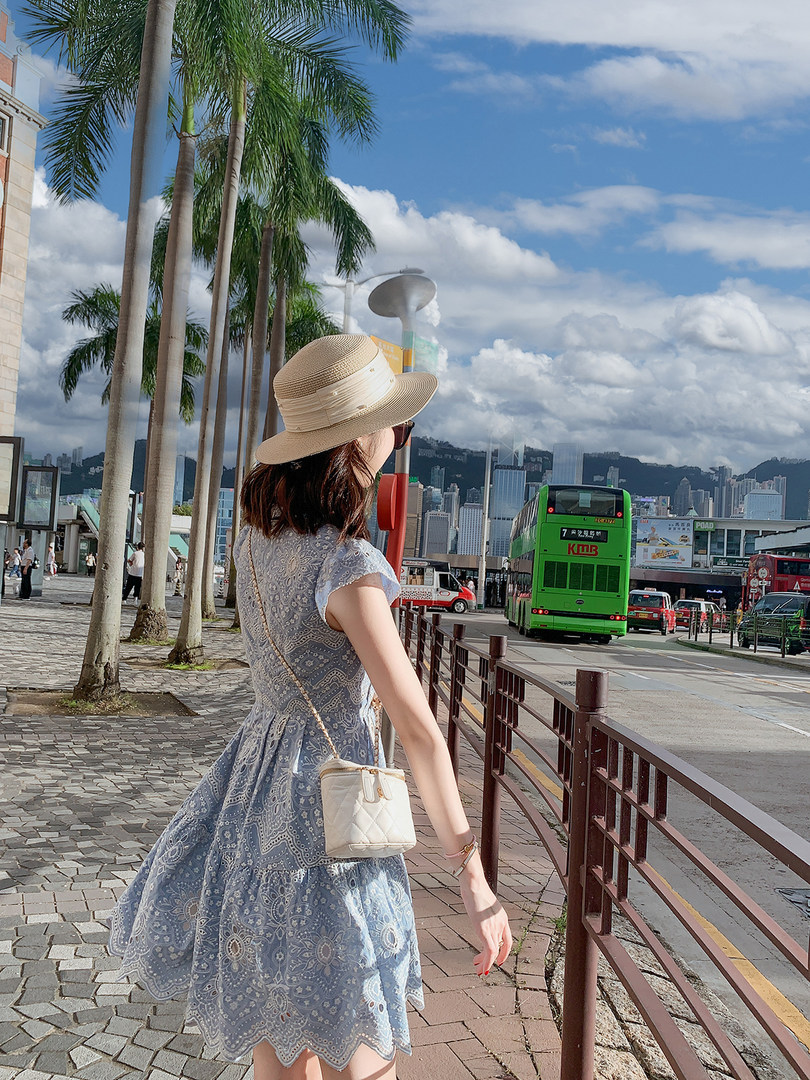 Woman wearing a blue lace dress with a straw hat and crossbody bag outdoors