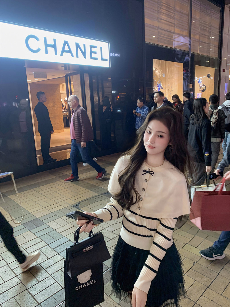 Woman wearing a cream and black striped sweater with a cape top in front of a Chanel store