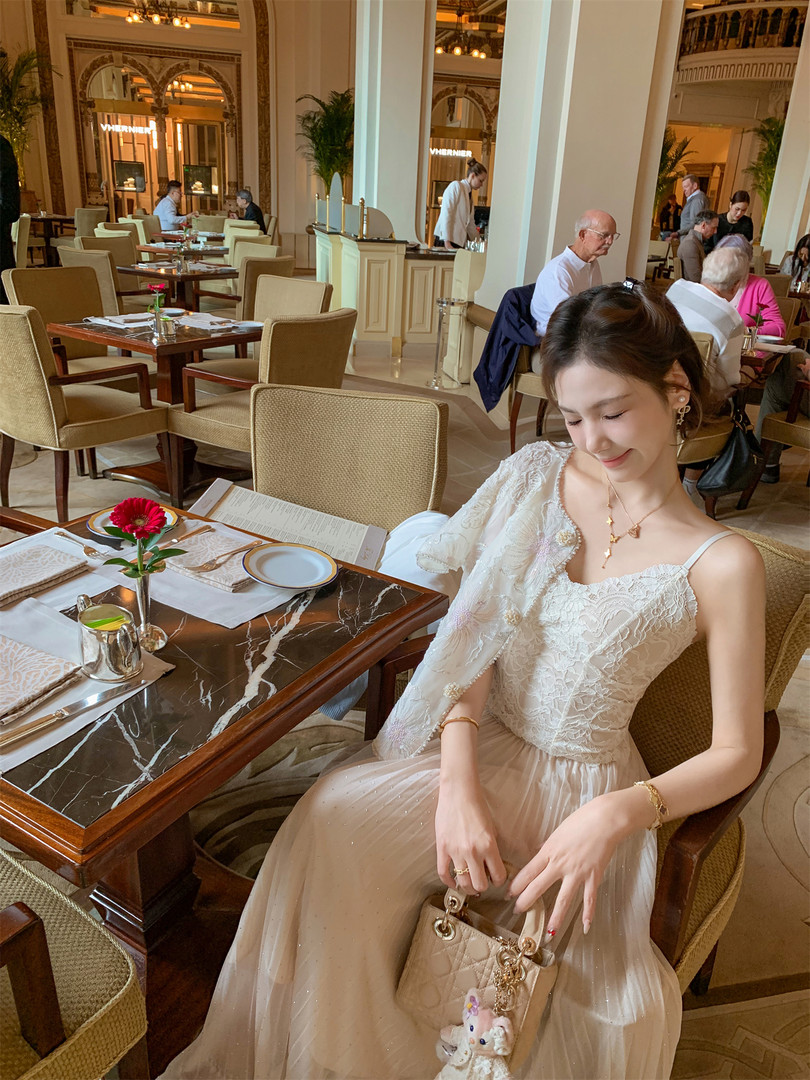 Woman wearing a white lace dress and holding a quilted beige handbag in a luxury restaurant