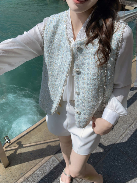 Woman wearing a light blue tweed vest over a white outfit by the water