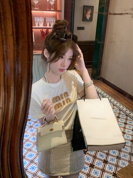 Woman wearing a white graphic T-shirt and carrying a small cream handbag