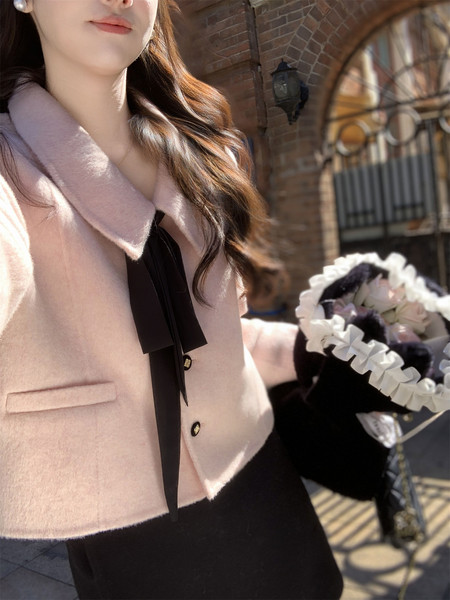 Model wearing a pale pink wool coat with black ribbon tie detail