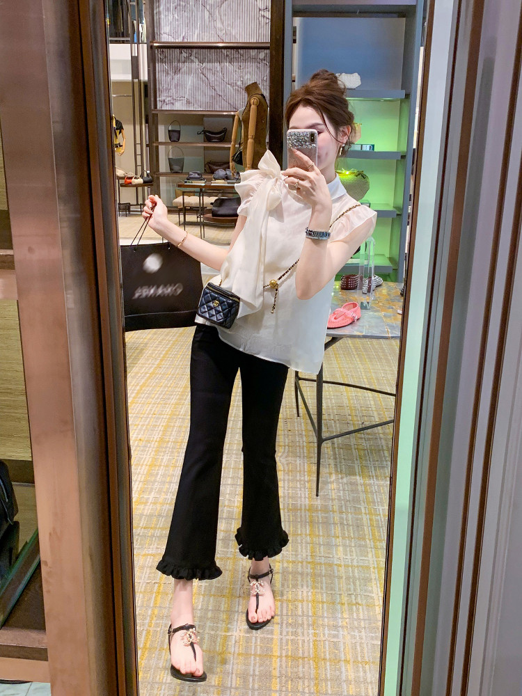 Woman wearing a white ruffled blouse with black cropped pants and sandals in a mirror selfie
