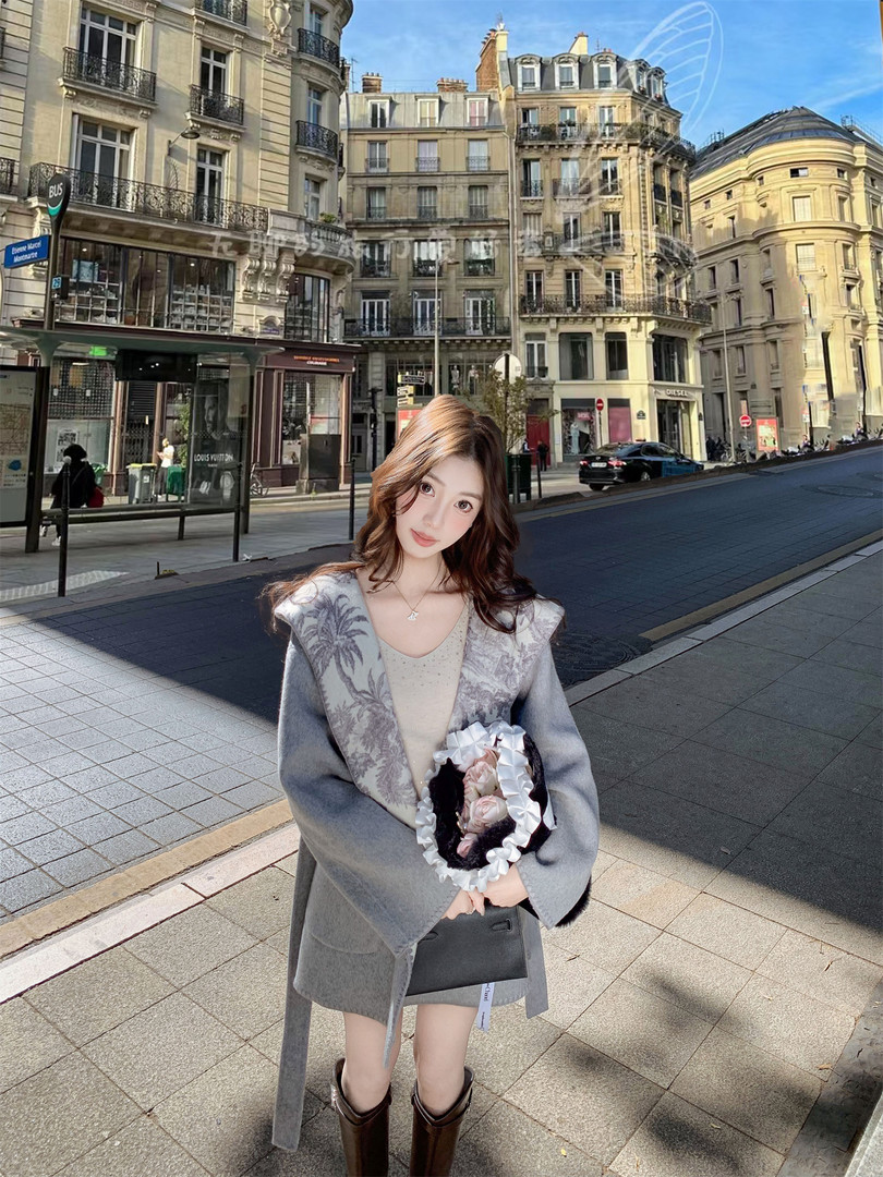 Woman wearing a gray belted coat and boots while holding a floral handbag on a city street