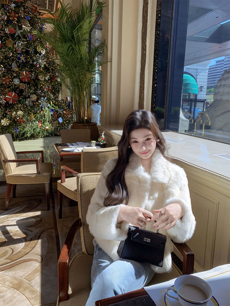 Woman wearing a white faux fur coat and holding a black handbag in a festive restaurant setting