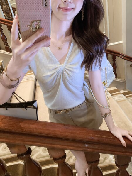 Woman wearing a white short-sleeve top and beige trousers in a mirror selfie