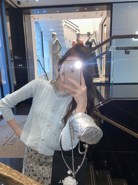 Mirror selfie of a woman wearing a white knit cardigan and carrying a silver quilted handbag