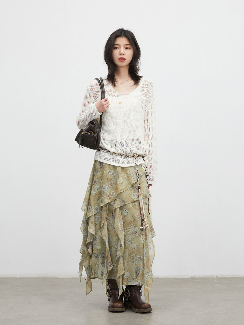 Model wearing a white knit top with a patterned layered skirt and brown boots, carrying a black shoulder bag
