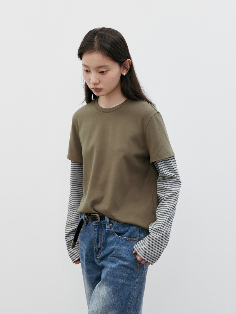 Model wearing an olive short-sleeve top layered over a striped long-sleeve shirt with blue jeans