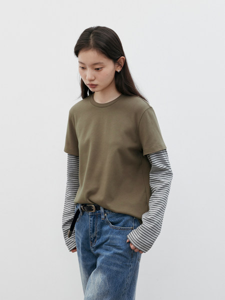 Model wearing an olive short-sleeve top layered over a striped long-sleeve shirt with blue jeans