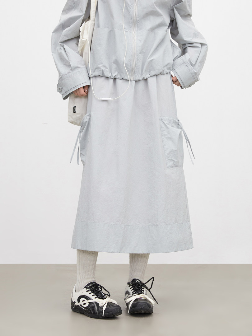 Model wearing a light gray jacket with matching long skirt and sneakers