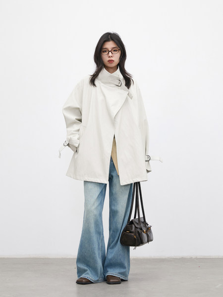 Model wearing a white oversized coat with wide-leg jeans and a black handbag