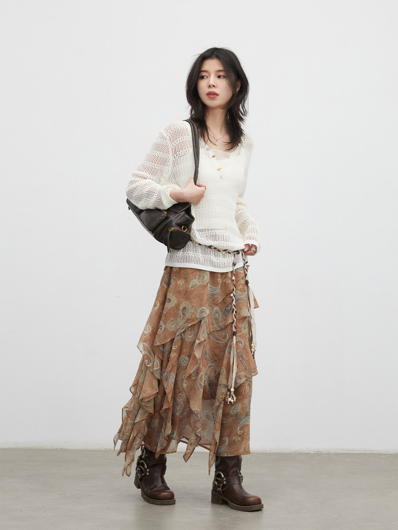 Model wearing a white knit sweater with a layered brown paisley skirt and dark boots