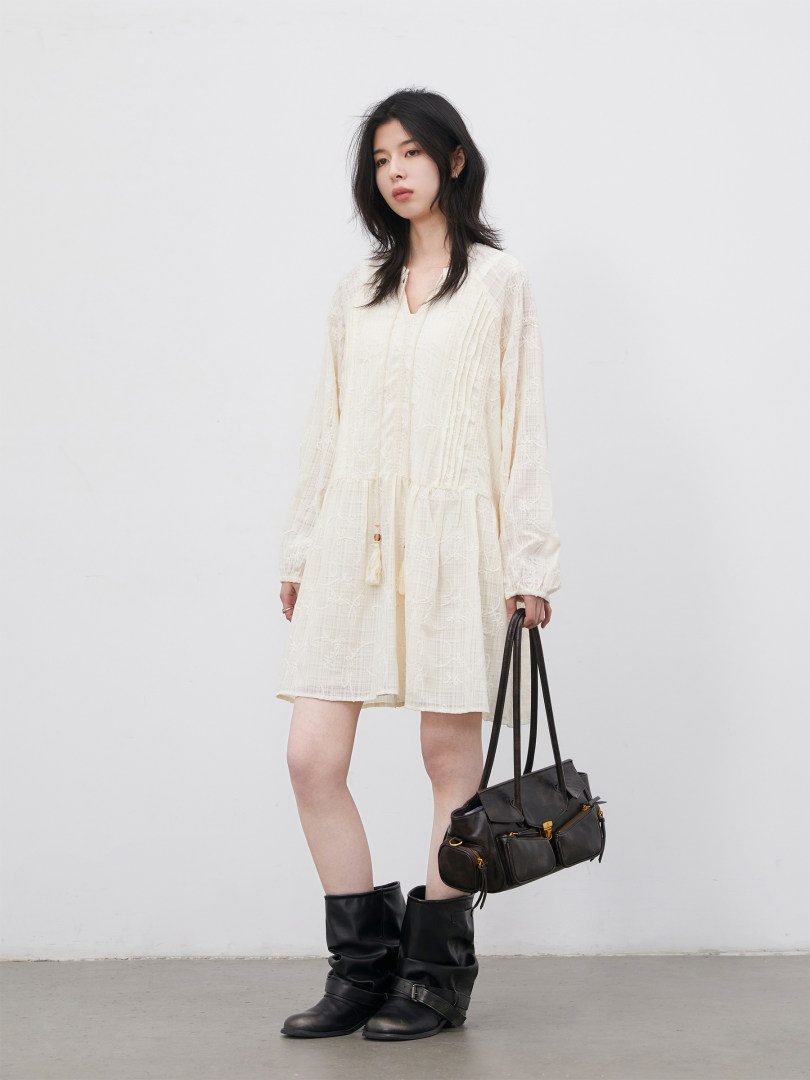Model wearing a cream long-sleeve mini dress with black boots and a black handbag
