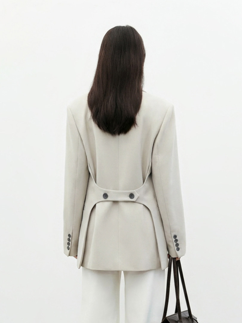 Model wearing a beige tailored blazer and matching trousers with a black handbag
