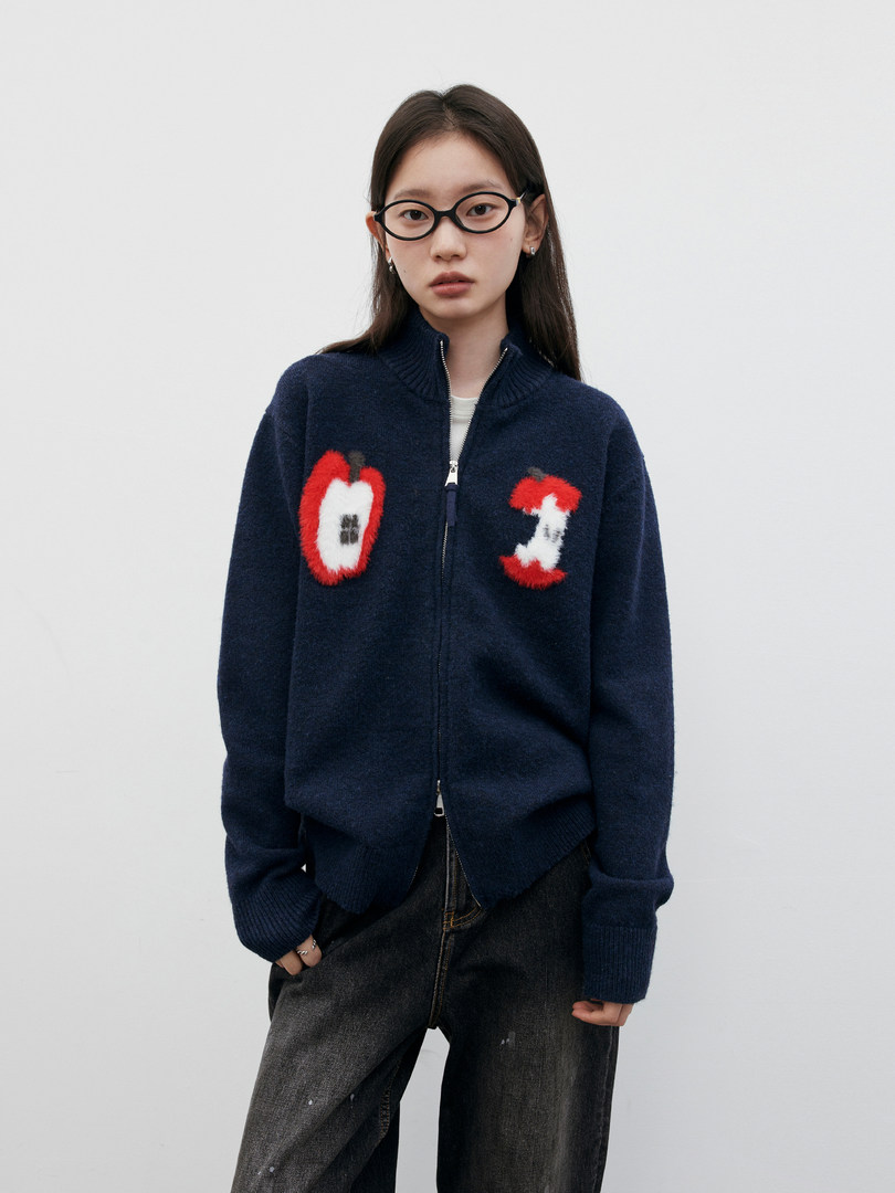 Model wearing a navy zip-up cardigan with apple graphics and dark jeans